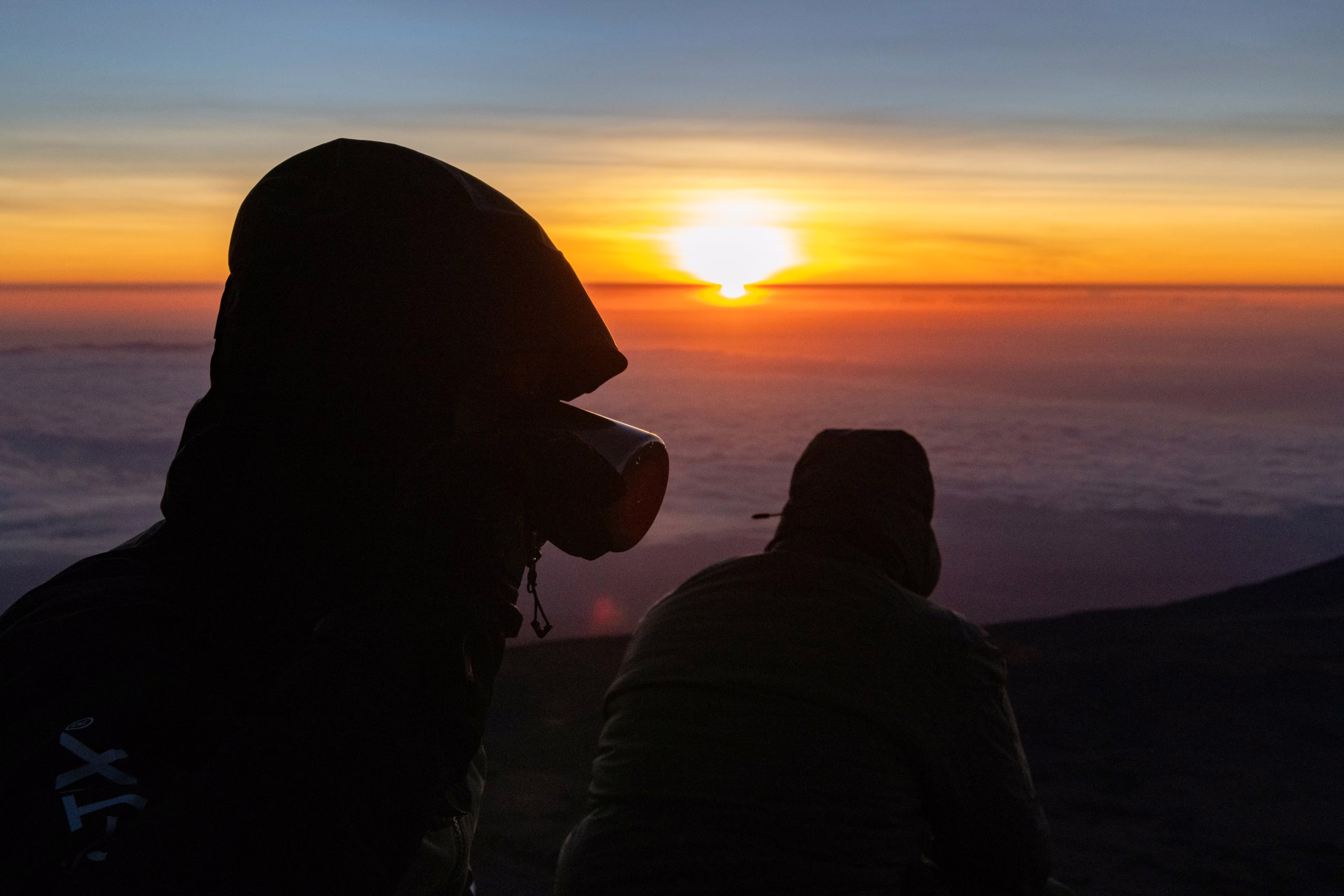 Deux silhouettes face au soleil, au-dessus de la mer de nuages